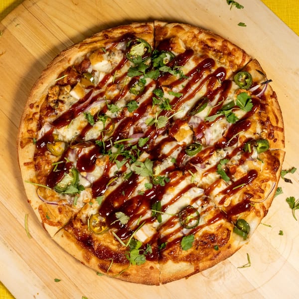 A BBQ chicken pizza with red onions, jalapeños, cilantro, and a drizzle of BBQ sauce.