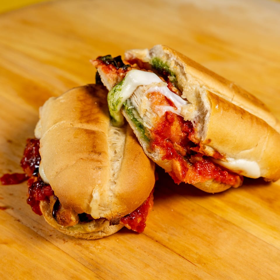 Two halves of a sandwich with melted cheese, red sauce, and green pesto on a wooden board.