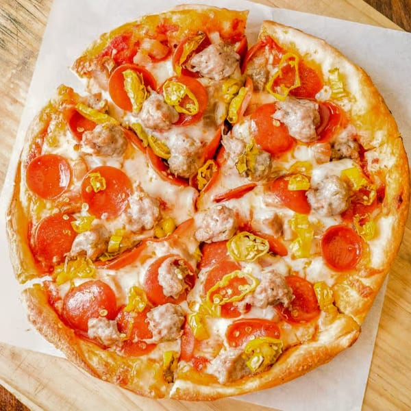 Totally Baked Pizza with pepperoni, sausage, and banana peppers on a wooden board.