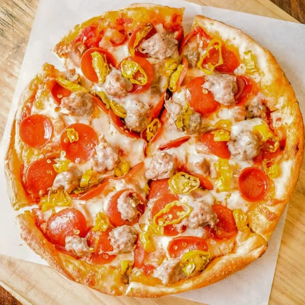 Totally Baked Pizza's pepperoni, sausage, and banana pepper pizza with a slice removed.