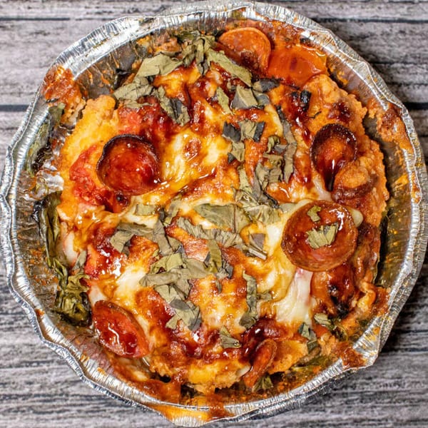 Totally Baked Pizza's baked pepperoni and cheese pizza with basil in a foil pan.